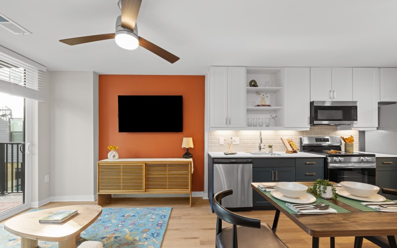 An interior view of a dining area, living room area, and a kitchen, with partial views of a patio sliding glass door at Trella Uptown pet-friendly apartments in Charlotte, NC.